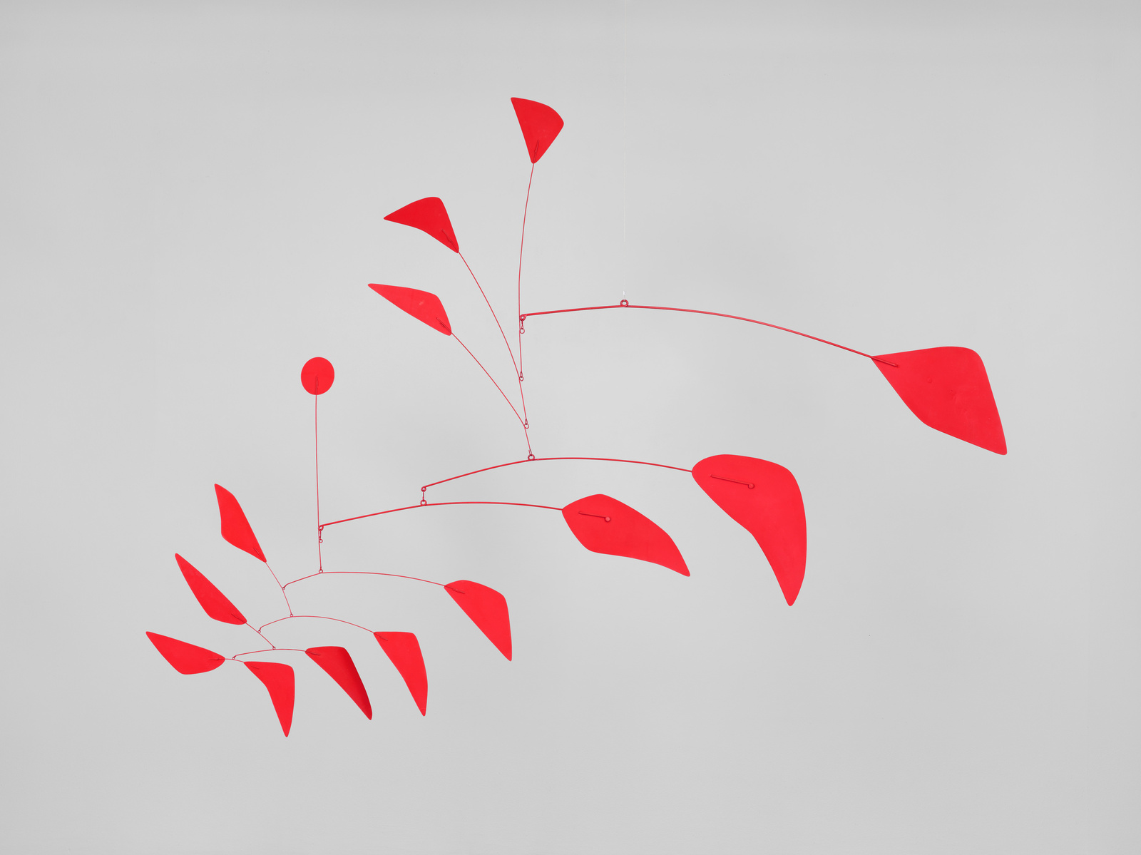 Red abstract mobile sculpture with various shapes hanging against a plain white background.