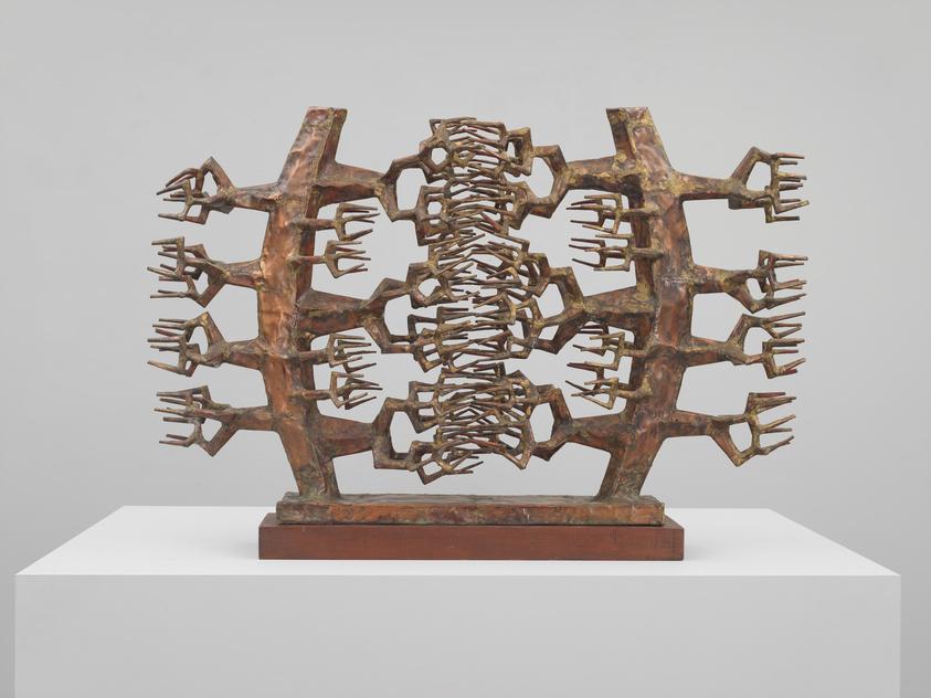 Bronze sculpture with interlocking geometric shapes and protruding elements, displayed on a white pedestal.