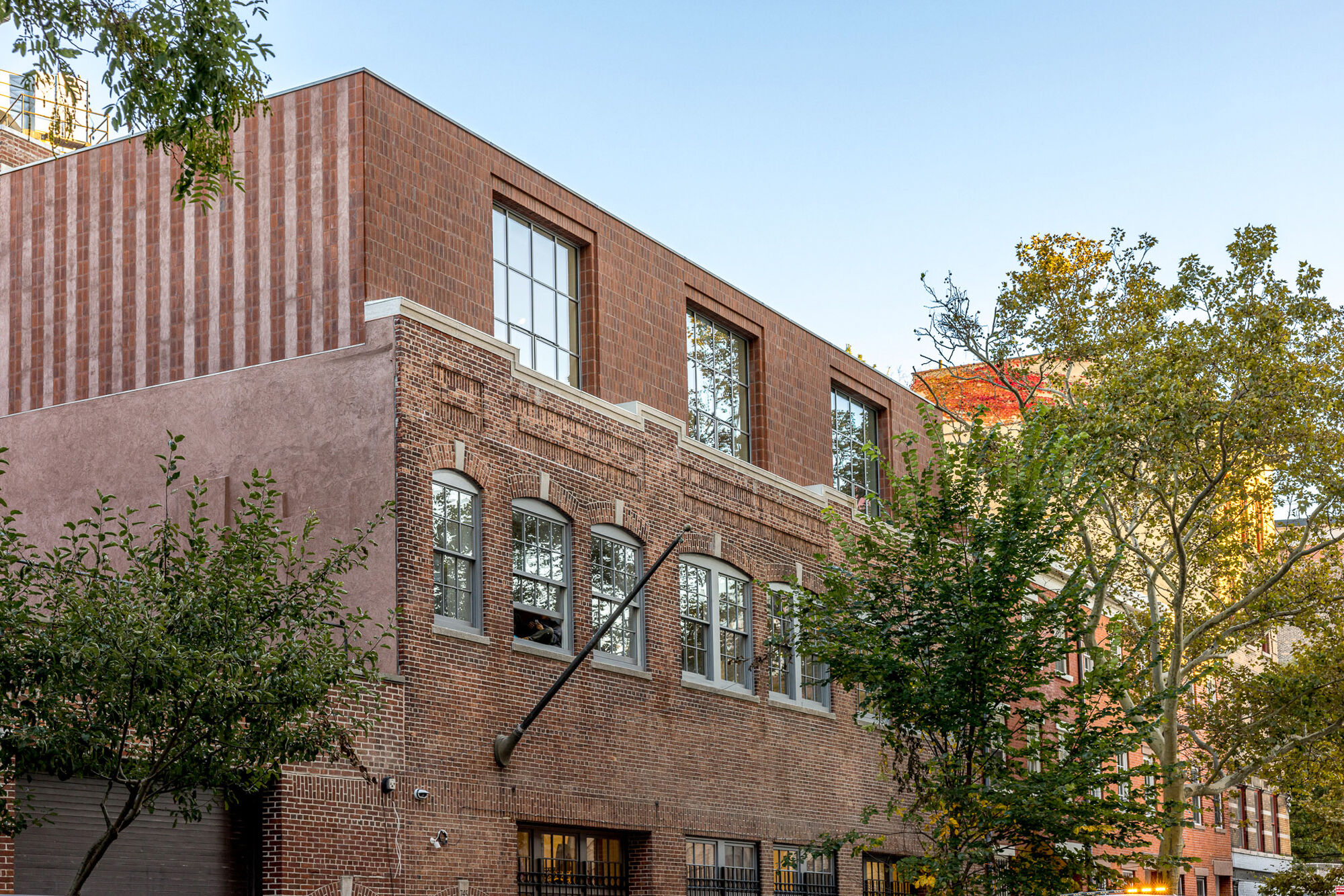 A three-floor brick building with leafy trees in front. 
