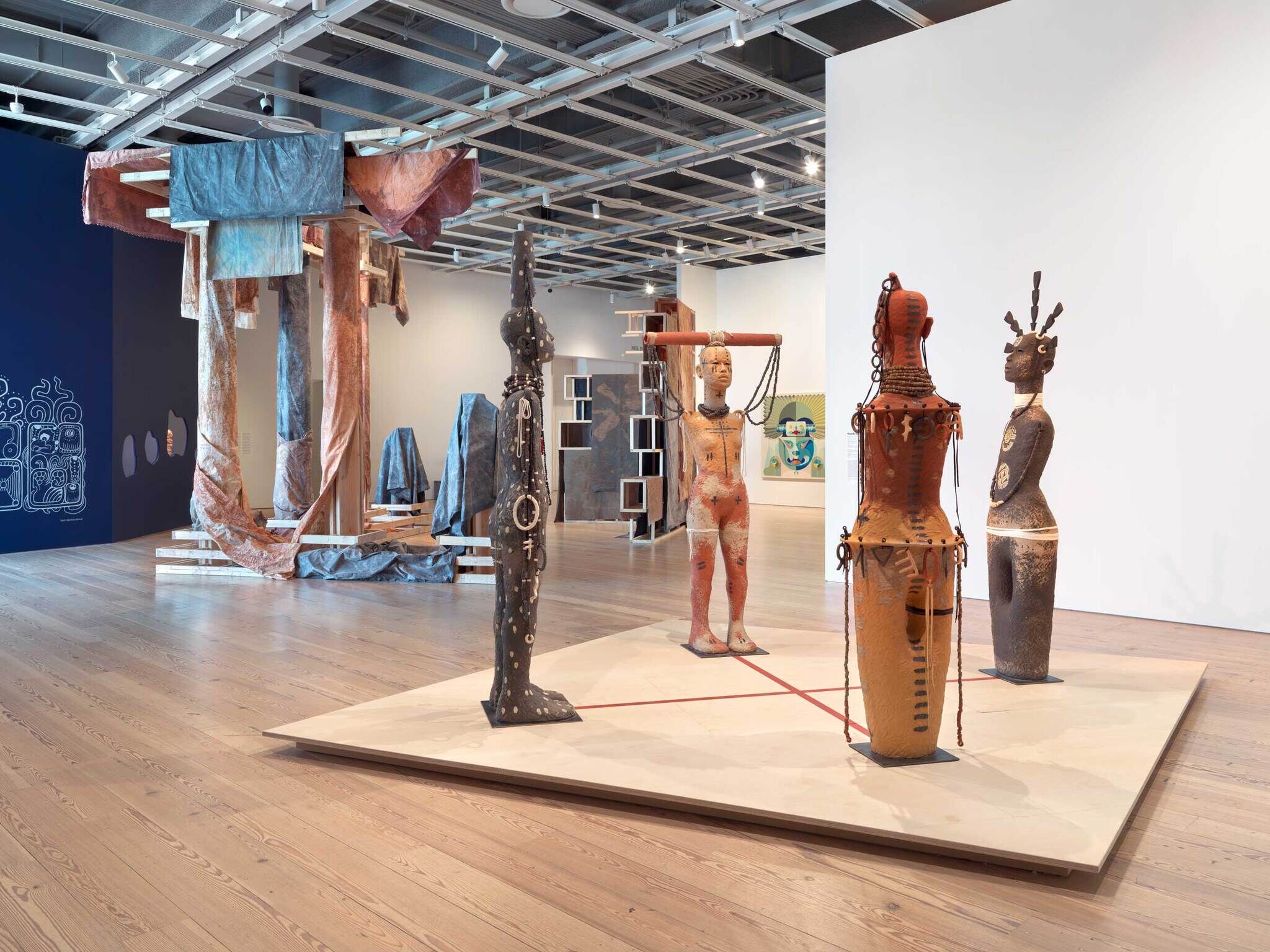 Modern art installation with abstract sculptures and draped fabrics in a gallery setting.